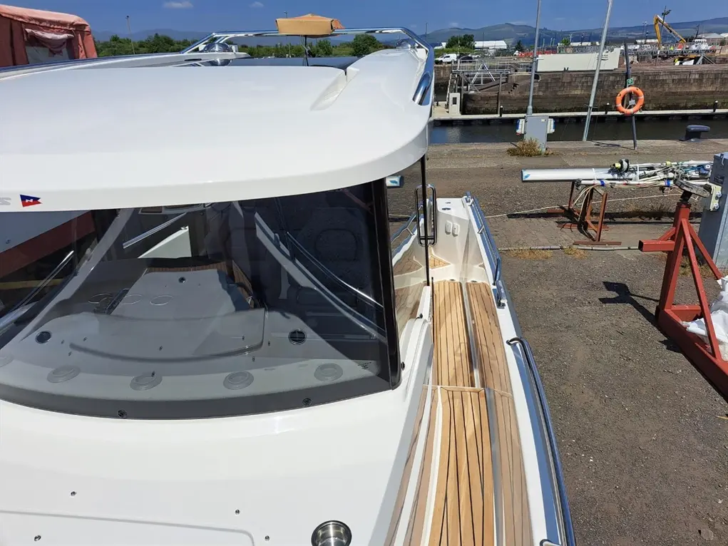 View from the deck of a white boat showing a wooden walkway and marina equipment in the background under a clear blue sky.